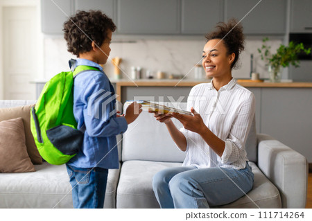Black mother gives son copybooks, preparing for school Black mother gives son copybooks, preparing for school 111714264