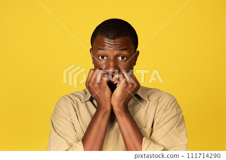 Shocked confused shy young black man in casual bites fingers Shocked confused shy young black man in casual bites fingers 111714290