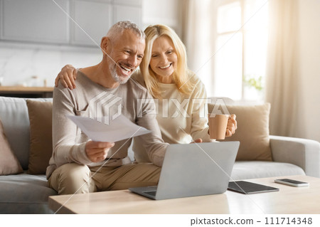 Happy couple of pensioners sitting using computer at home Happy couple of pensioners sitting using computer at home 111714348