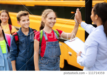 Black teacher lady giving high-fives to kids boarding the school bus 111714359