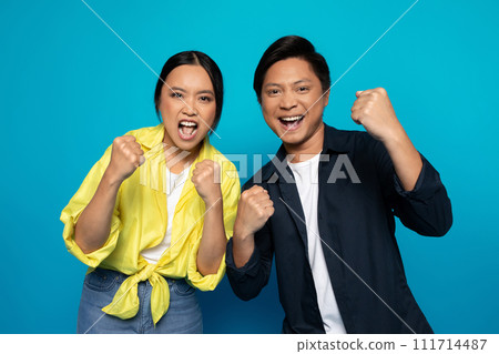 Glad excited young asian man and woman in casual rise fists, celebrate victory 111714487