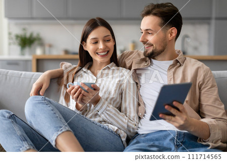 Happy young couple sharing digital tablet and woman holding cup of coffee 111714565