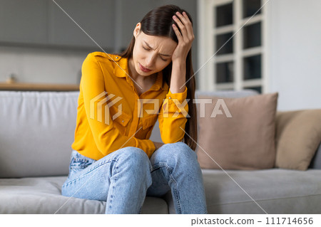 Stressed young woman with headache sitting on the couch 111714656