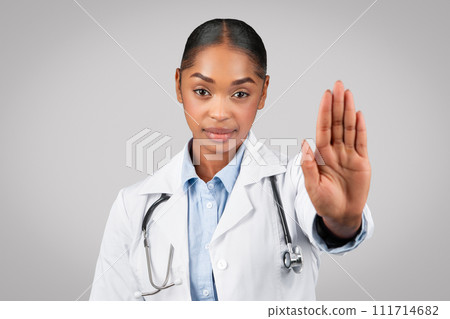 Confident calm young african american lady doctor in white coat make stop sign with hand Confident calm young african american lady doctor in white coat make stop sign with hand 111714682