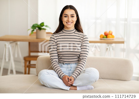 Smiling calm pretty young arab lady sit on sofa, enjoy free time, peace 111714729