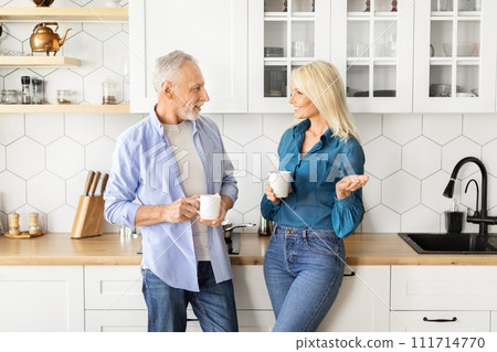 Smiling senior man and woman drinking coffee together in modern kitchen interior Smiling senior man and woman drinking coffee together in modern kitchen interior 111714770