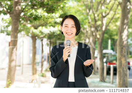 Female announcer with microphone outdoors Female announcer with microphone outdoors 111714837