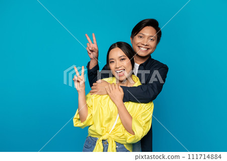Smiling young korean guy hug lady in casual show peace sign with hands, enjoy relationships 111714884