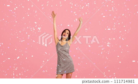 Vibrant young woman in a glittery dress with a wide smile, arms joyfully raised Vibrant young woman in a glittery dress with a wide smile, arms joyfully raised 111714981