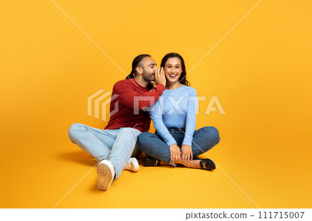 Man sharing secrets with girlfriend, millennial couple on yellow 111715007