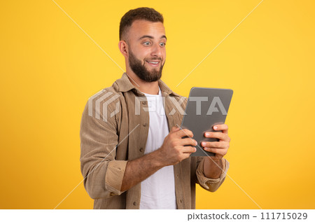 Shocked funny european millennial man with beard look at tablet, using app for social networks Shocked funny european millennial man with beard look at tablet, using app for social networks 111715029