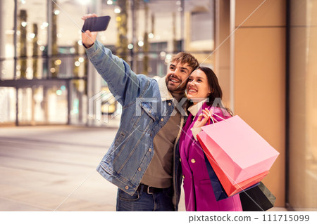 Millennial couple joyfully taking a selfie on smartphone outside mall 111715099