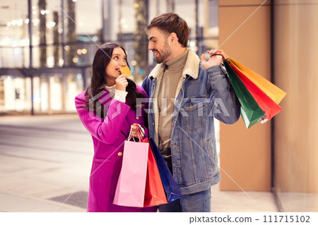 Young woman excitedly shows credit card to boyfriend outside mall Young woman excitedly shows credit card to boyfriend outside mall 111715102