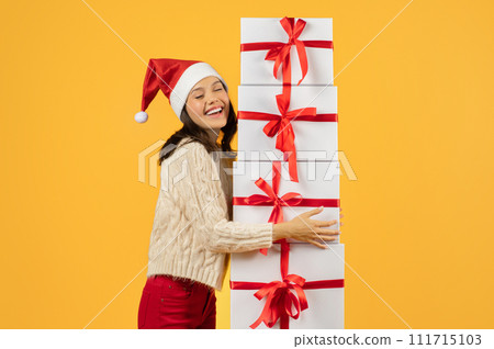 Cheerful woman embracing stack of Christmas gifts on yellow backdrop Cheerful woman embracing stack of Christmas gifts on yellow backdrop 111715103