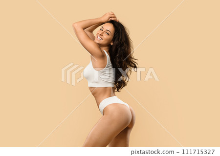 Attractive young woman in white underwear playfully posing against beige background Attractive young woman in white underwear playfully posing against beige background 111715327