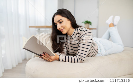 Happy calm young pretty arab woman read book, planning work, lie at sofa Happy calm young pretty arab woman read book, planning work, lie at sofa 111715356