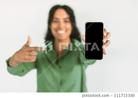 Black woman showcases cellphone blank screen pointing over white backdrop 111715380
