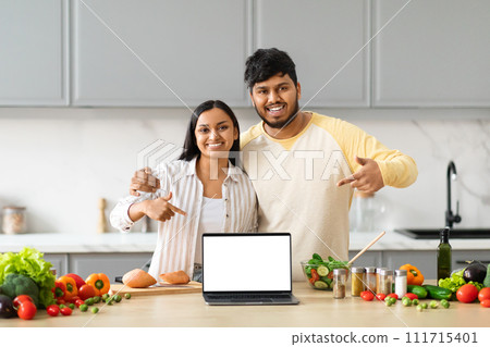 Positive young indian couple cooking at home, showing laptop Positive young indian couple cooking at home, showing laptop 111715401