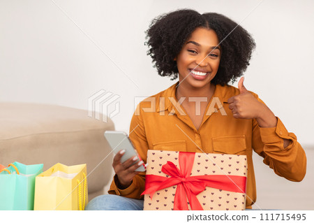 African American woman with a joyful smile looking at her phone and giving a thumbs up 111715495