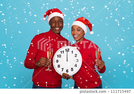 Couple In Santa Hats Holding Champagne Glasses And Clock, Studio Couple In Santa Hats Holding Champagne Glasses And Clock, Studio 111715497