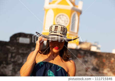 Beautiful woman wearing the traditional Colombian hat called Sombrero Vueltiao at the Clock Tower on the historical streets of the Cartagena de Indias walled city Beautiful woman wearing the traditional Colombian hat called Sombrero Vueltiao at the Clock Tower on the historical streets of the Cartagena de Indias walled city 111715846