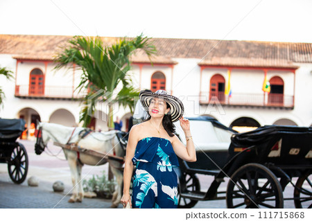 Beautiful woman wearing the traditional Colombian hat called Sombrero Vueltiao at the Customs Square on the historical streets of the Cartagena de Indias walled city 111715868