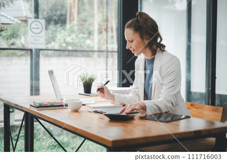 Business woman concept, A dedicated professional is immersed in work, writing in a notebook with a laptop and tablet on her well-organized office desk. Business woman concept, A dedicated professional is immersed in work, writing in a notebook with a laptop and tablet on her well-organized office desk. 111716003