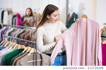 Dreamy female in casual outfit holding a pink buttonless jacket while shopping in a mall 111716206
