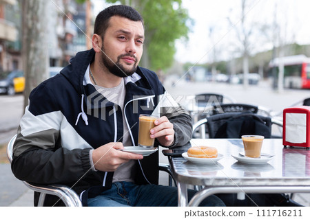 Young man traveler enjoying cocoa with donut in street cafe Young man traveler enjoying cocoa with donut in street cafe 111716211