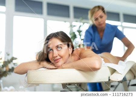 Relaxed young woman receiving back massage from skilled masseuse Relaxed young woman receiving back massage from skilled masseuse 111716273