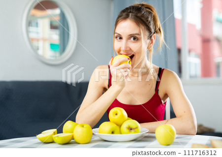 Portrait of young woman sitting at table and eating apples Portrait of young woman sitting at table and eating apples 111716312