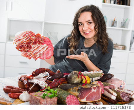 Woman costs near table on which sausages and smoked meat Woman costs near table on which sausages and smoked meat 111716378