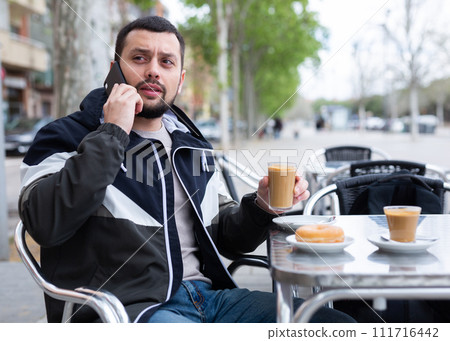 Young man talking on phone during breakfast in street cafe 111716442