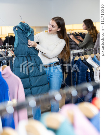 Young woman choosing insulated vest in store Young woman choosing insulated vest in store 111716510