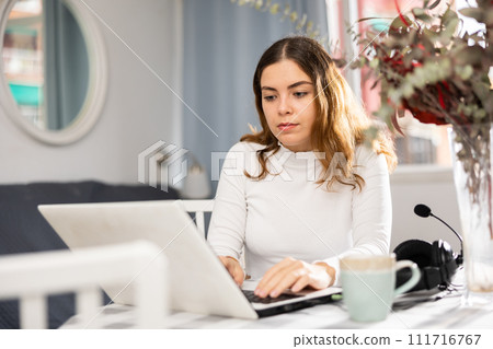 Young woman sitting at table and using laptop 111716767
