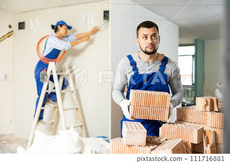 Repairman in coverall carrying bricks during apartment renovation Repairman in coverall carrying bricks during apartment renovation 111716881