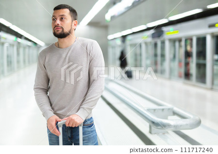 Young man standing with suitcase on subway station platform Young man standing with suitcase on subway station platform 111717240