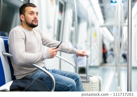 Young man with suitcase and phone traveling in subway car Young man with suitcase and phone traveling in subway car 111717261