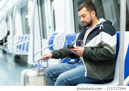 Bearded traveler sitting with suitcase and smartphone in metro car 111717264