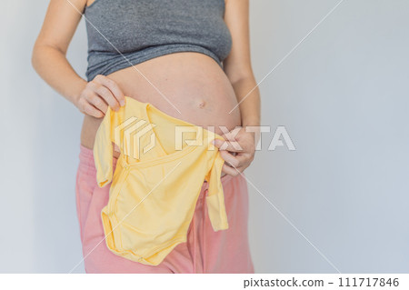 In a tender moment of anticipation, a pregnant woman cradles her unborn baby's clothes in her hands, savoring the sweetness of preparing for the little one's arrival 111717846