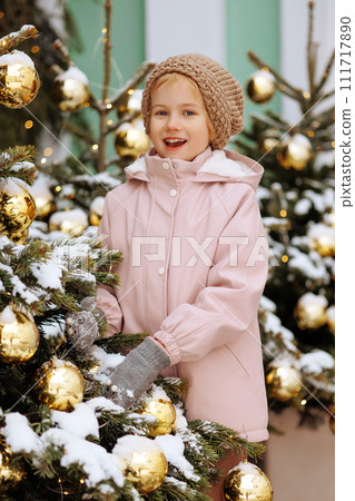 Child in a coat near a snow-covered Christmas tree 111717890
