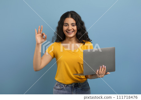 Positive young indian woman holding and using laptop Positive young indian woman holding and using laptop 111718476