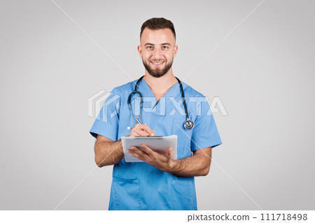 Smiling nurse writing on a clipboard in blue scrubs Smiling nurse writing on a clipboard in blue scrubs 111718498