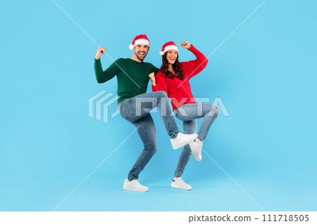 Couple In Santa Hats Shaking Fists Over Blue Studio Background Couple In Santa Hats Shaking Fists Over Blue Studio Background 111718505