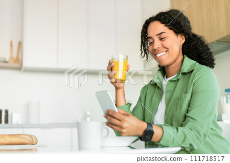 black woman looking at phone, drinking fresh orange juice indoor 111718517