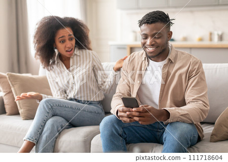 Discontented Black Wife Looking At Husband Browsing On Phone Indoor 111718604