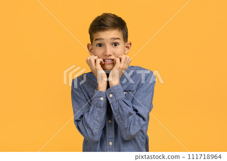 Anxious teenage boy in denim shirt biting nails and looking at camera Anxious teenage boy in denim shirt biting nails and looking at camera 111718964