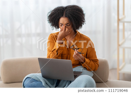 An overwhelmed African American woman with a laptop pinches the bridge of her nose An overwhelmed African American woman with a laptop pinches the bridge of her nose 111719046