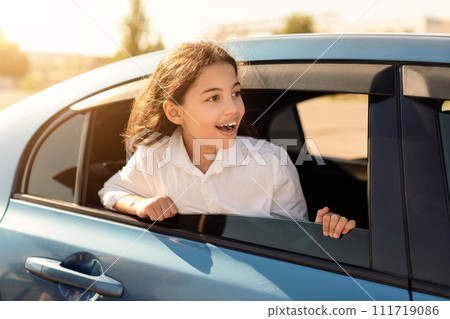 Excited young girl peeking out from car window Excited young girl peeking out from car window 111719086