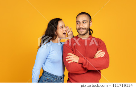 Young woman sharing secret with her husband, yellow background Young woman sharing secret with her husband, yellow background 111719134